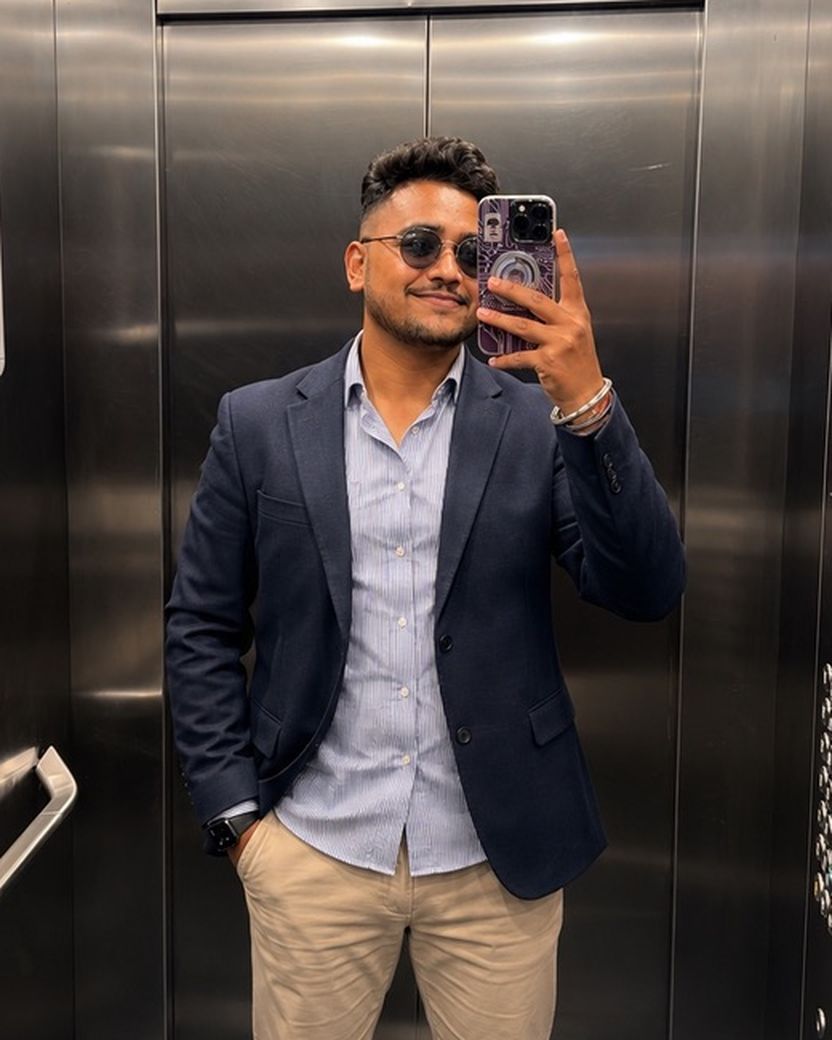 Suraj Shaw in a navy blazer and sunglasses, taking a mirror selfie in a steel lift